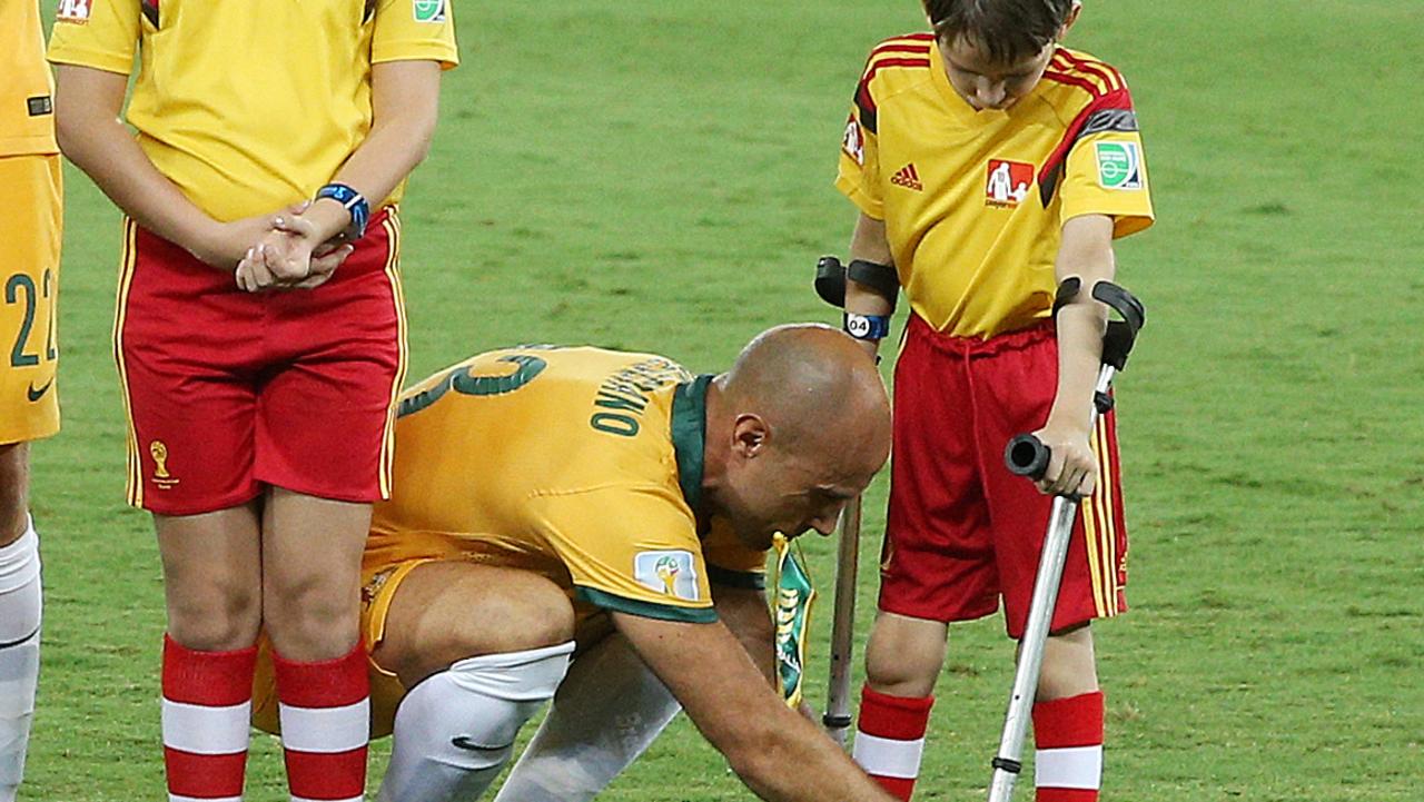 Australia V's Chile at Arena Pantanal, Group B in the 2014 World Cup, 13th June, Cuiaba, Brazil. Australia's Mark Bresciano comes out with a boy on crutches and help him tie up his shoe laces. Pic : George Salpigtidis