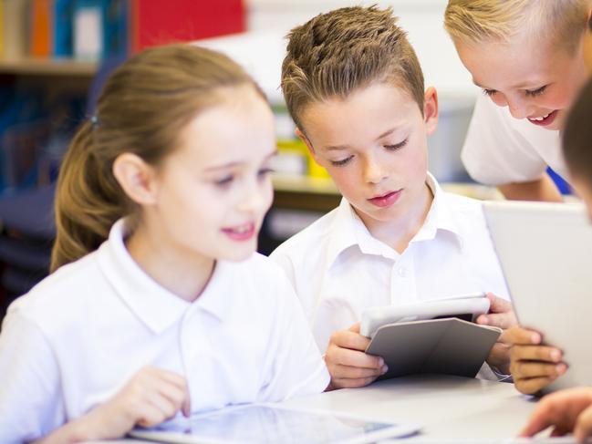 Happy students in classroom using a digital tablet, they are all wearing uniforms.