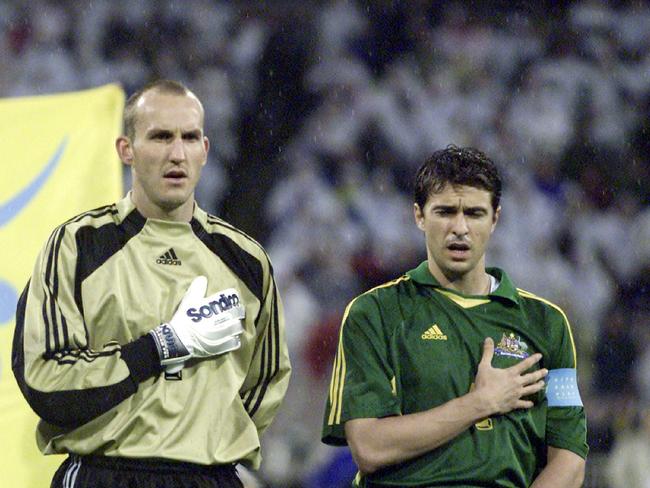 Former Socceroos Mark Schwarzer and Paul Okon with their hands on their chests during the national anthem.