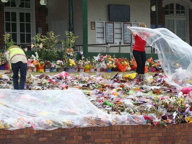 Red Cross volunteers cover the floral tributes with plastic to protect them from rain. Picture by Scott Fletcher