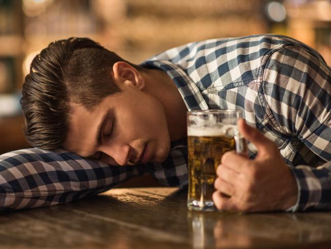Young exhausted drunk man holding a glass of beer and sleeping on the table in the pub.