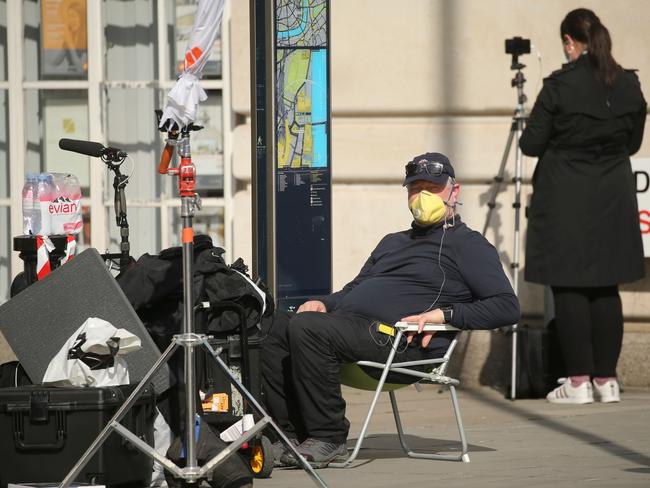 A journalist wearing a mask sits on the pavement opposite St Thomas’ Hospital in central London, where Boris Johnson is receiving treatment in intensive care. Picture: AFP