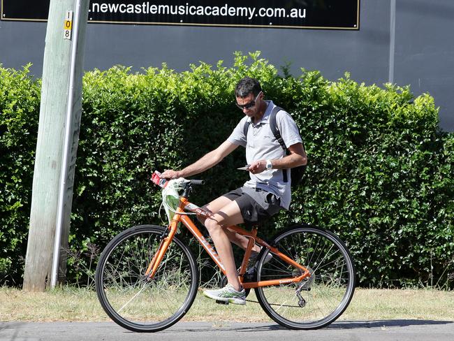 A cyclist rides along King Street Newcastle with no helmet on his mobile phone. Picture by Peter Lorimer.
