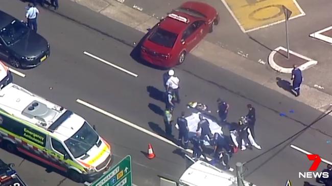 The man’s body lies covered in the middle of the road, with the carjacked red taxi nearby. Picture: 7 News