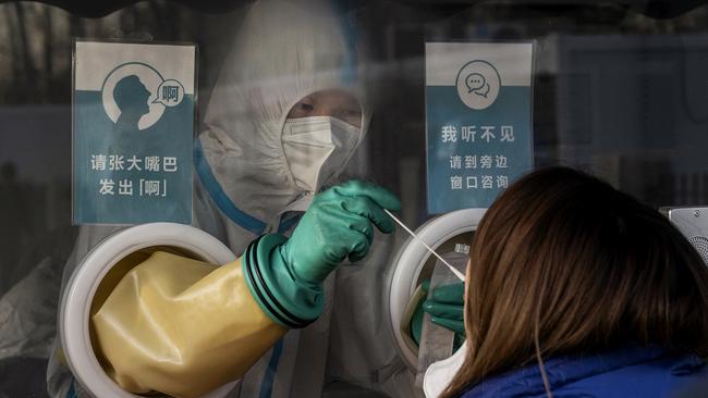 A medical worker reaches through protective gloves as she administers a nucleic acid test to a client at a private outdoor clinic in Beijing, China, this week. Picture: Getty Images