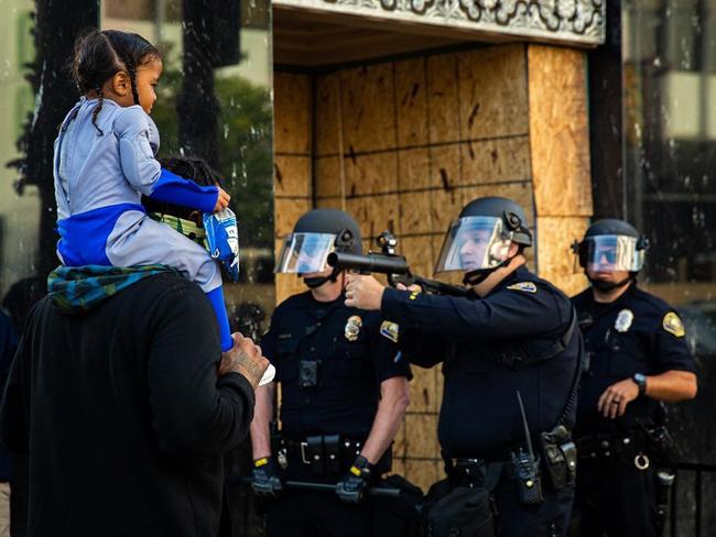 Freelance photographer Richard Grant took this photo of a policeman with pointing a rubber bullet gun in front of a man and a child during protests at Long Beach, California. Picture: Richard Grant