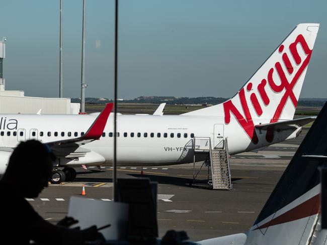 A man sits at a cafe in front of a Virgin Australia aircraft at Sydney Airport, Sydney, Friday, June 19, 2020. (AAP Image/James Gourley) NO ARCHIVING