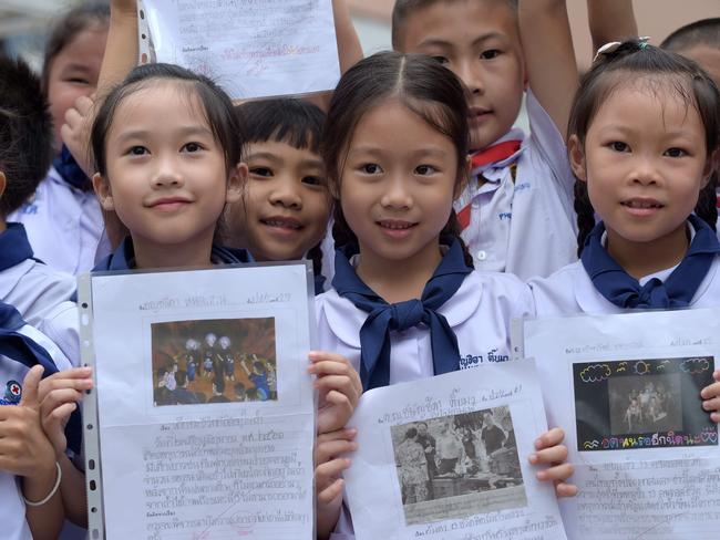 Thai students smile as they hold pictures of 12 boys and a football coach at a school in front of hospital where the boys rescued after being trapped. Picture: AFP