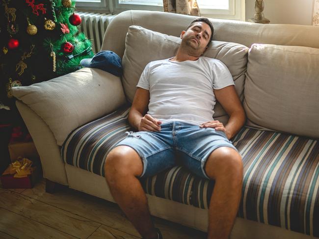 Tired young man sleeping on a couch in the living room during Christmas.