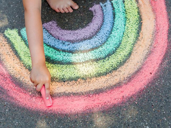 the child girl draws a rainbow with colored chalk on the asphalt. Child drawings paintings concept. Education and arts, be creative when back to school