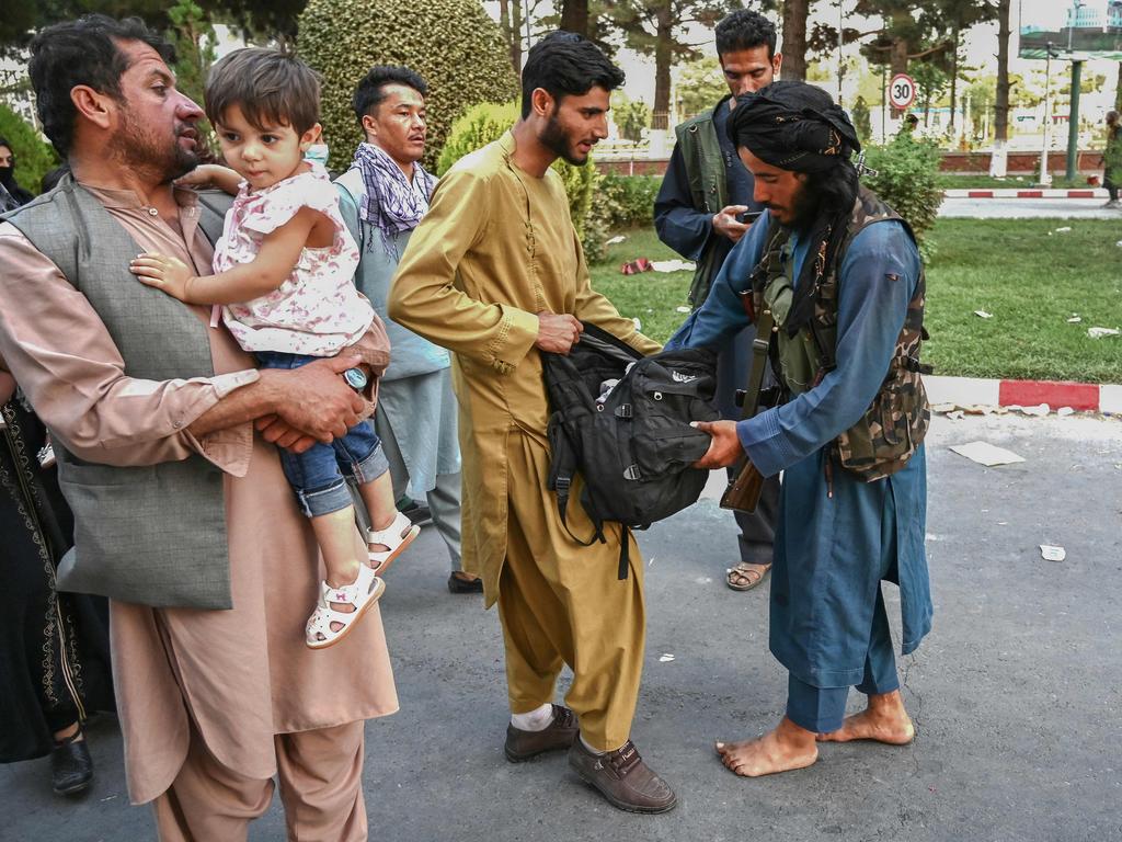 A Taliban fighter, right, searches the bags of people at Kabul Airport. Picture: Wakil Kohsar / AFP