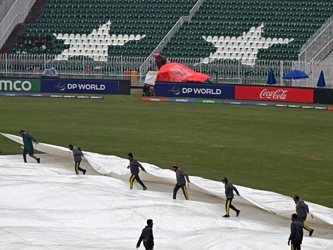 Groundmen cover the pitch as it rains before the start of the ICC Champions Trophy one-day international (ODI) cricket match between Australia and South Africa at the Rawalpindi Cricket Stadium in Rawalpindi on February 25, 2025. (Photo by Farooq NAEEM / AFP)