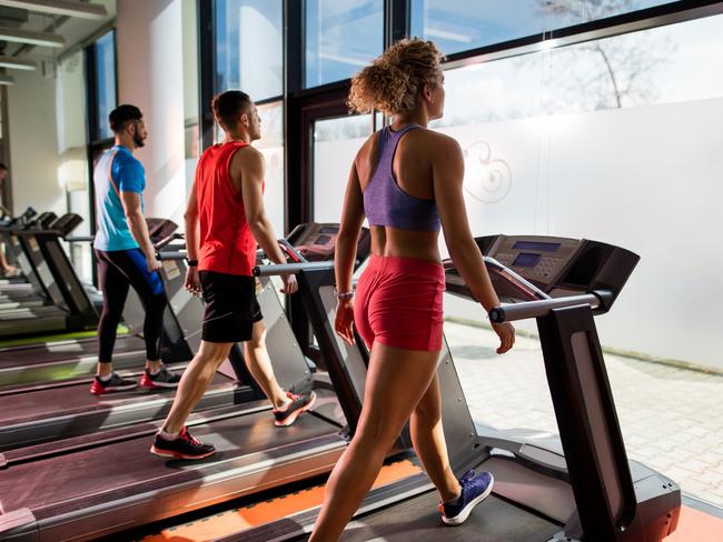 Team of young people exercising in health club while walking on treadmills.  Focus is on young woman.