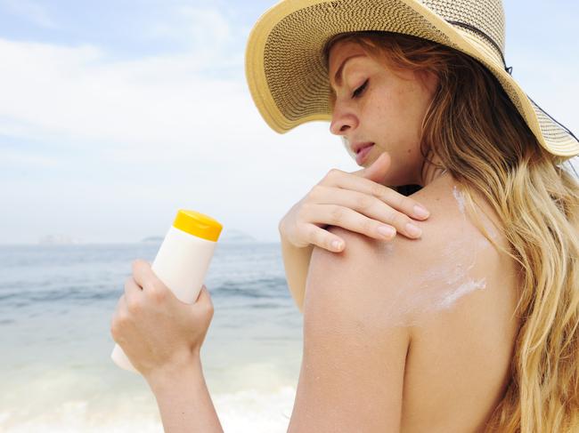 woman applying suntan lotion at the beach smiling