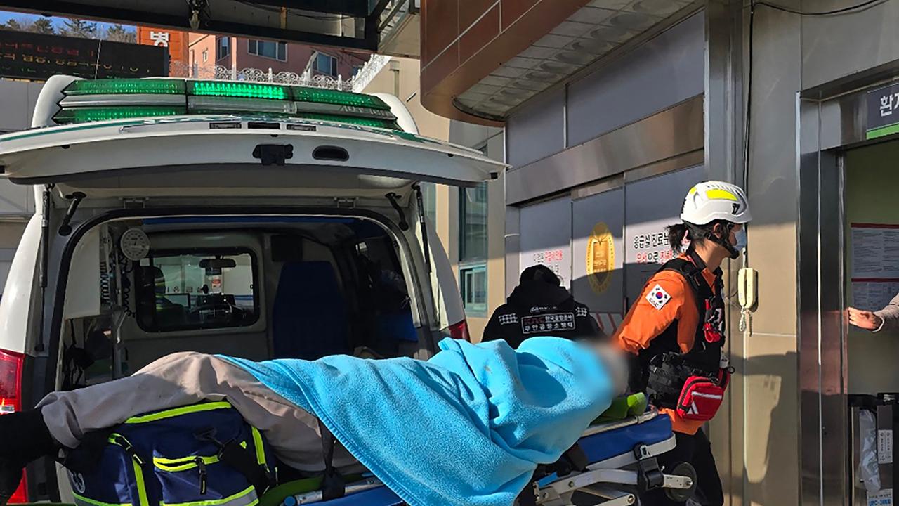 A passenger (face digitally blurred at source) is transferred from an ambulance to a medical facility following the crash. Picture: AFP