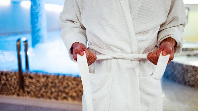 Cropped photo of a male standing near the pool while tying the belt of his towelling robe. Picture: iStock/ljubaphoto