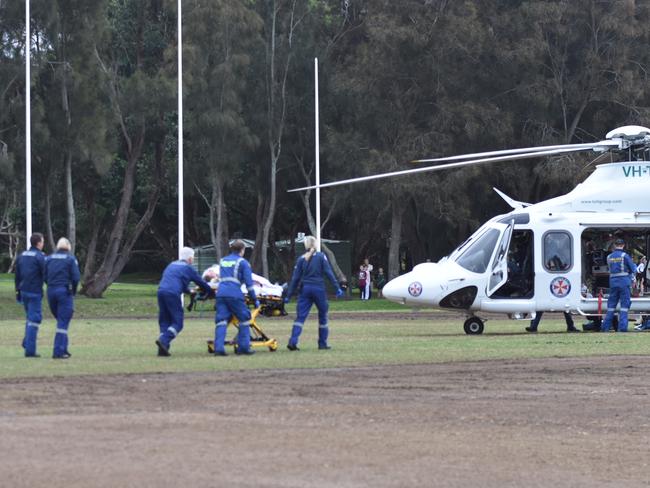 NSW Ambulance paramedics at Weldon Oval, Curl Curl, treat a men who suffered a serious head injury after falling from a wheelie bin in the grandstand. Picture: Sebastien Dekker