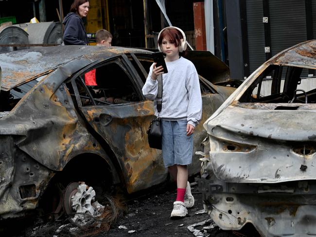 A girl listens music as she walks past burned out vehicles parked outside a shopping mall following a night-time drone attack on Kyiv. Picture: AFP
