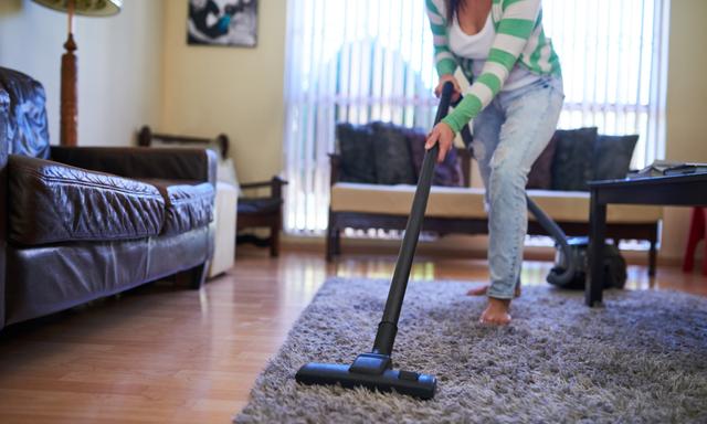 Shot of a young woman vacuuming a carpet at home
