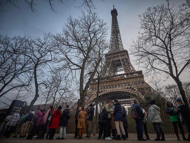 Tourists walk next to the Eiffel Tower at sunrise as the monument is shut due to a staff strike over the financial management of the monument by the city, closing the monument to the public during the second week of the French school holidays, in Paris on February 19, 2024. Unions of the operating company of the Eiffel Tower, the CGT and Force Ouvriere say the city, which owns 99 percent of the tower, has underestimated costs and overestimated revenues, whilst also hinting to the threat of a strike during the Olympic Games, held in Paris from July 26 to August 11. (Photo by Kiran Ridley / AFP)