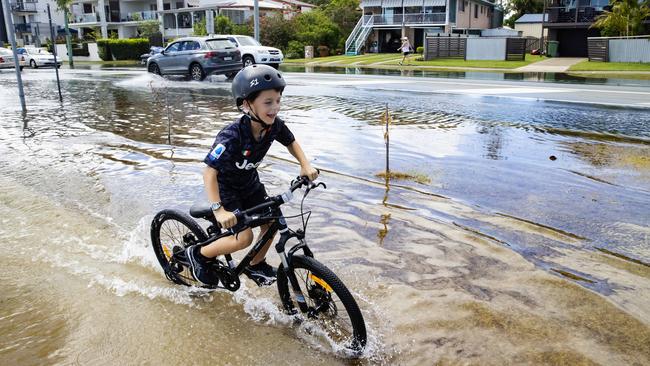 Nine-year-old Timer Vincent rides his bike through the king tide on Bradman Ave at Maroochydore. Picture: Lachie Millard