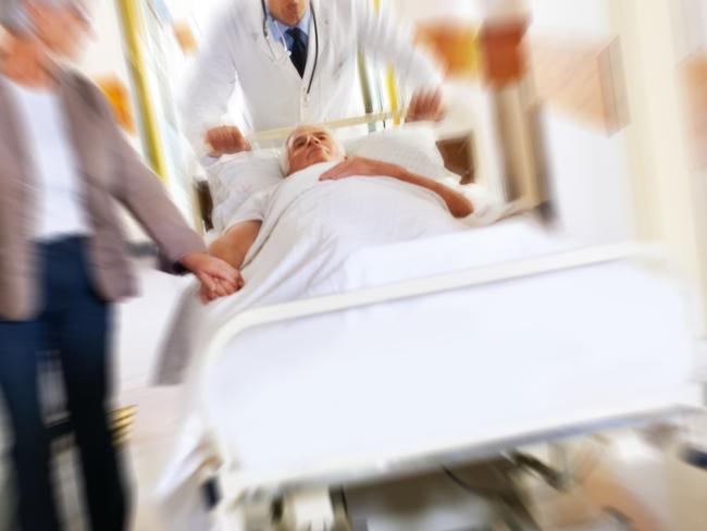 Shot of a sick man on a bed being wheeled at speed through a hospital corridor with his wife at his side Emergency ward. Picture: istock