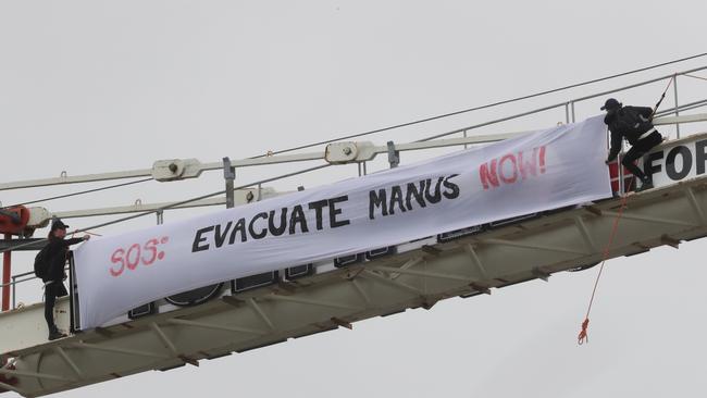 Protesters climb a crane to display a banner regarding refugees on Manus Island. Photo: AAP