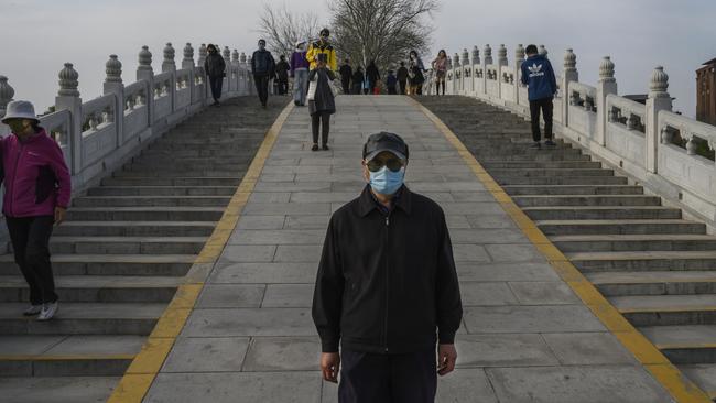 People wear protective masks as they cross a footbridge while enjoying the spring weather at a park in Beijing, China. Picture: Getty Images