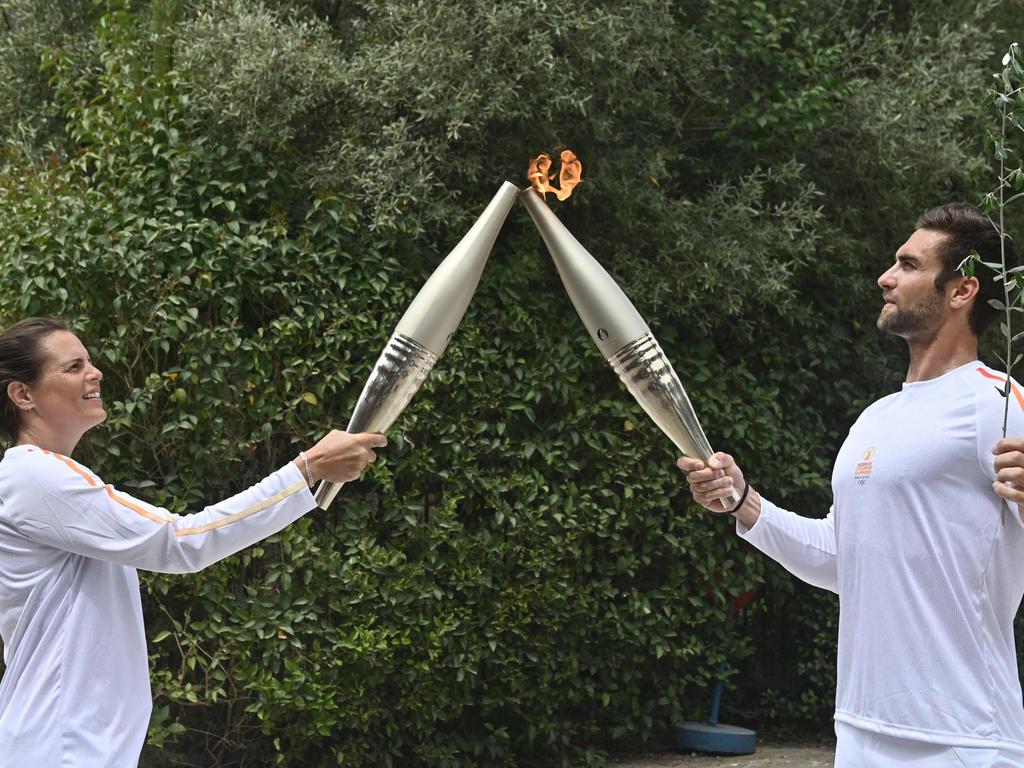 Olympic rowing gold medallist for Greece in 2020, Stefanos Ntouskos, right, lights the torch held by French Olympic swimming champion Laure Manaudou, the first torchbearer from host nation France. Picture: Valerie Gache/AFP