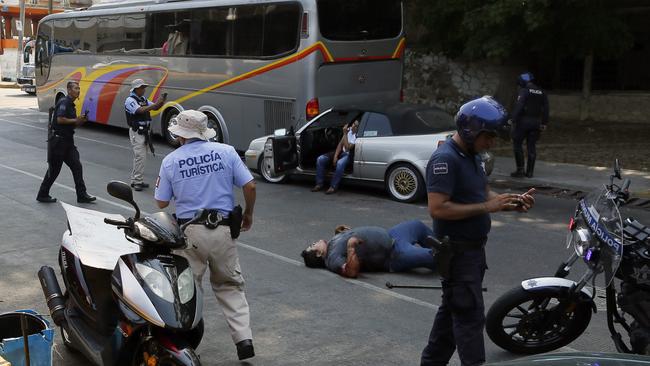 A wounded man lies on the ground and a second one sits in his car waiting for assistance as police arrive to the scene of a shooting near Caleta Beach in Acapulco. Picture: AP Photo/Enric Marti