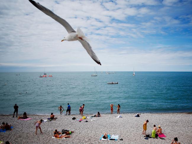 A seagull flies over beachgoers on the coast at Étretat, north-western France on July 17, 2018. / AFP PHOTO / CHARLY TRIBALLEAU