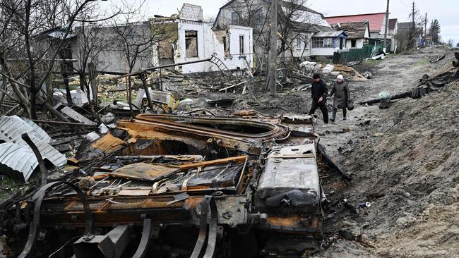 Local residents walk amid debris of a charred Russian tank next to destroyed houses in the village of Zalissya, northeast of Kyiv, last month. Picture: AFP