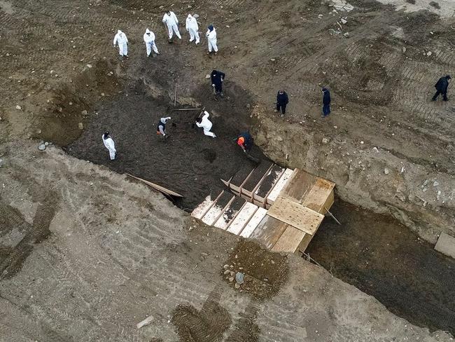 Workers wearing personal protective equipment bury bodies in a trench on Hart Island, New York City, April 9. Picture: AP Photo/John Minchillo