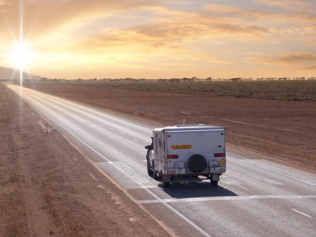 An Australian Outback touring caravan on the road in the early morning near Eucla, on the Western/South Australia border. The markings on the road show it is a Flying Doctor landing strip.