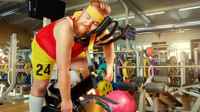 A fat man is tired on a simulator in the gym.