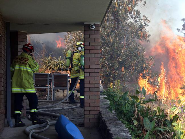 Firefighters monitor flames close to a home in North Curl Curl. Picture: David Swift.