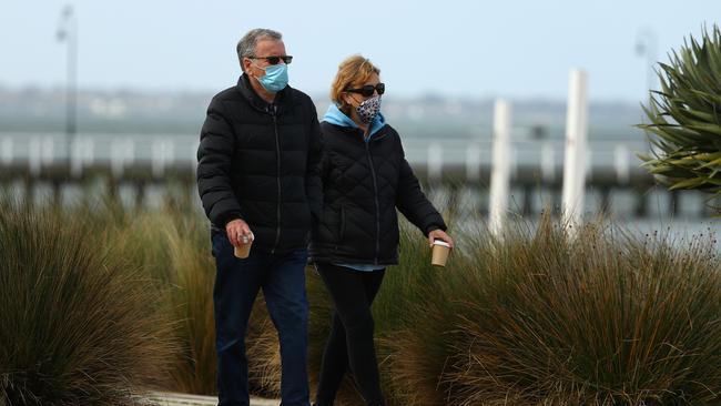 People walk along Port Melbourne Beach wearing masks.