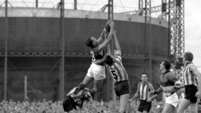 Footscray footballer Ted Whitten taking a mark in front of the gasometer.