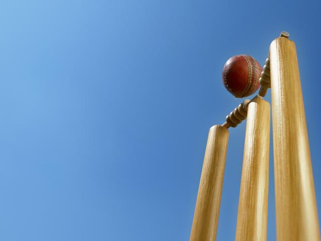 Close-up of cricket ball hitting the stumps and knocking off the bails against sky.