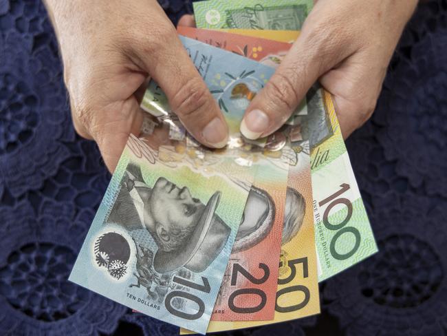 Female adult (45-49 years) holding some Australian bank notes on a blue background. This visual concept evokes ideas around saving money, paying for expenses and investments.