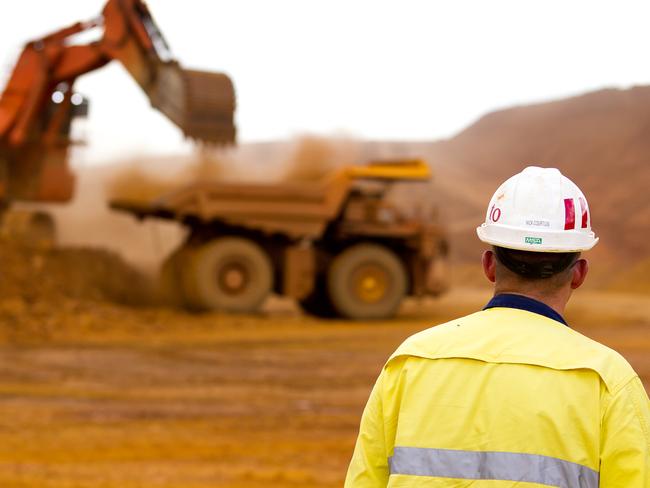 A mine worker watches as a haul truck is loaded by a digger with material from the pit at Rio Tinto Group's West Angelas iron ore mine in Pilbara, Australia, on Sunday, Feb. 19, 2012. Rio Tinto Group, the world's second-biggest iron ore exporter, will spend $518 million on the first driverless long-distance trains to haul the commodity from its Western Australia mines to ports, boosting efficiency. Photographer: Ian Waldie/Bloomberg