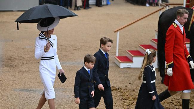 Catherine shelters from the rain with an umbrella as she walks with her children. Picture: AFP