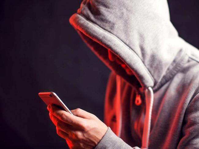 Man wearing hoody sweater with mobile phone in hands. Crime and hacking concept; scam generic.