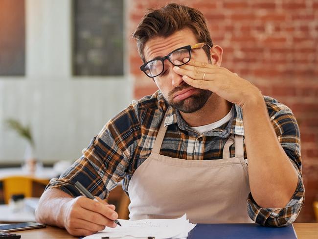 CAREERS: exhausted young business owner doing admin at a table in his coffee shopStressed cafe owner.Picture: iStock