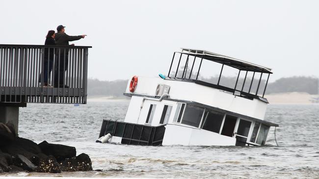 Walkers stop and look at a sunken houseboat washed up by the wild weather on the banks of the Broadwater Parklands at Southport on the Gold Coast on Friday. Picture: Glenn Hampson.