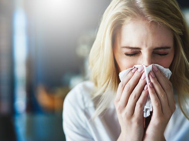 Shot of a frustrated businesswoman using a tissue to sneeze in while being seated in the office