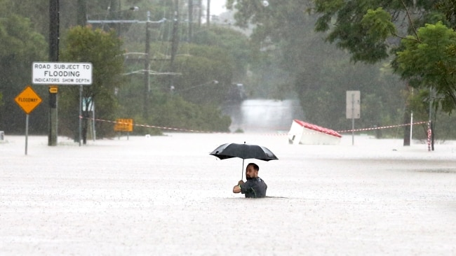 A man walking through chest-high floodwaters in Queensland as emergency services warn of flooding danger. Picture: Steve Pohlner