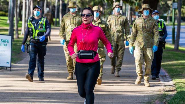 A woman is seen jogging around the Tan running track as she passes Australian Defence Force (ADF) personnel and Protective service officers as they walk on patrol on August 06, 2020 in Melbourne, Australia. Picture: Asanka Ratnayake/Getty Images