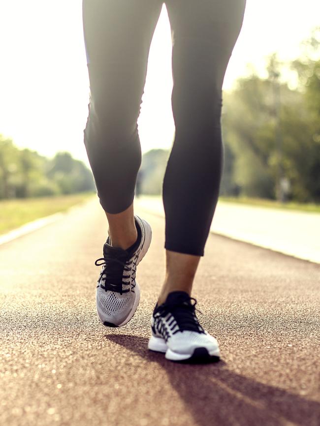 Unrecognisable muscular man running or walking on track field, low angle view of his running shoes.