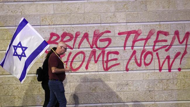 An Israeli couple holding their national flag walk in front of graffiti calling for the release of Israeli hostages held in the Gaza Strip. Picture: AFP.